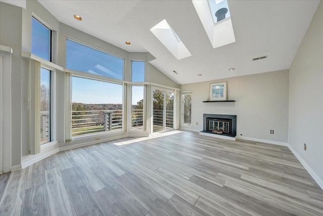 unfurnished living room featuring a skylight, visible vents, a glass covered fireplace, wood finished floors, and high vaulted ceiling