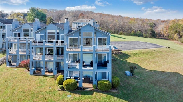 rear view of property featuring a patio, a balcony, and a lawn