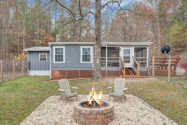 rear view of house featuring a sunroom, a yard, and a fire pit