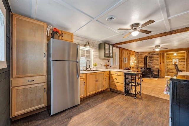 kitchen with sink, a wood stove, stainless steel fridge, wooden walls, and dark hardwood / wood-style flooring