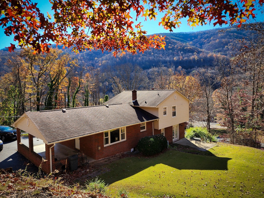 exterior space with brick siding, a forest view, a shingled roof, a chimney, and a yard