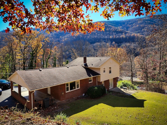 exterior space with brick siding, a forest view, a shingled roof, a chimney, and a yard