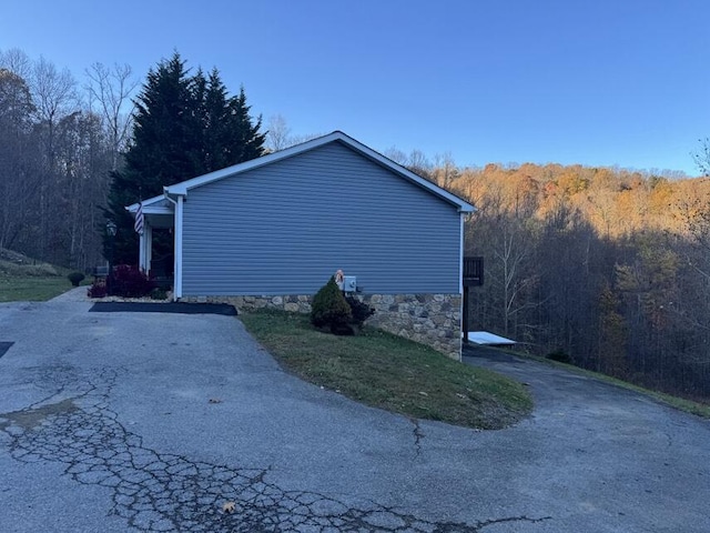 view of side of property featuring aphalt driveway and a forest view