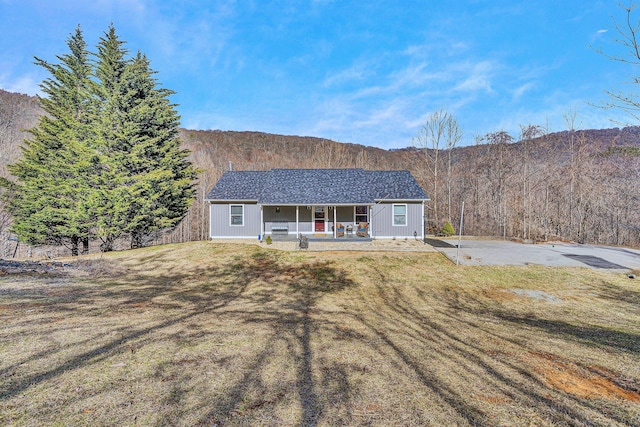 ranch-style home with a porch, a view of trees, and a front lawn