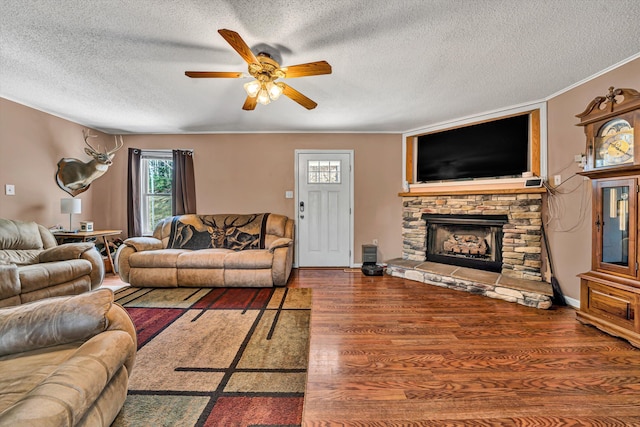 living room featuring wood finished floors, a fireplace, ornamental molding, ceiling fan, and a textured ceiling