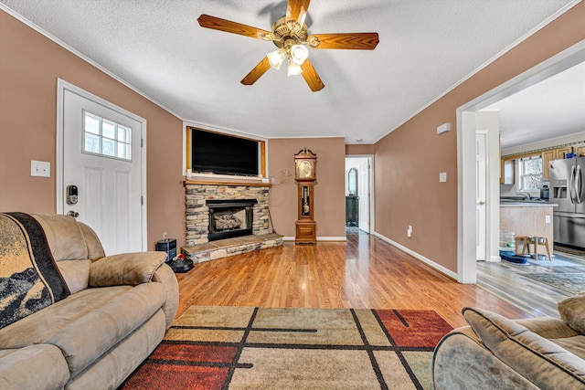 living room featuring a textured ceiling, ornamental molding, a fireplace, and light wood finished floors