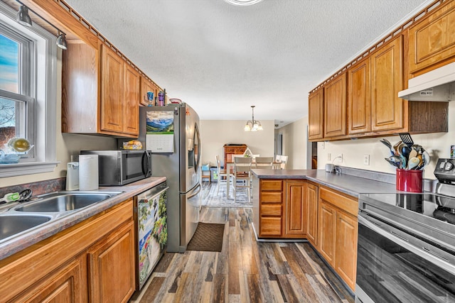 kitchen featuring brown cabinetry, a peninsula, dark wood-style flooring, stainless steel appliances, and under cabinet range hood