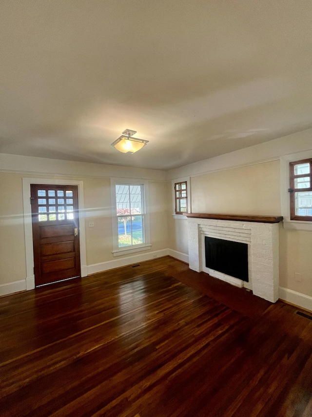 unfurnished living room featuring dark hardwood / wood-style floors, a brick fireplace, and a wealth of natural light