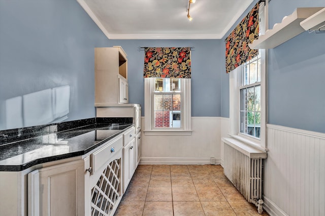 kitchen featuring white cabinets, crown molding, dark stone countertops, light tile patterned floors, and radiator heating unit