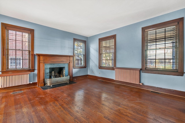 unfurnished living room featuring hardwood / wood-style flooring, a healthy amount of sunlight, and radiator heating unit