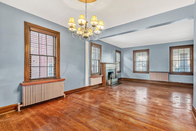 unfurnished living room with hardwood / wood-style floors, beam ceiling, radiator heating unit, and an inviting chandelier