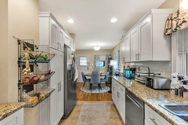 kitchen featuring decorative backsplash, light stone countertops, stainless steel appliances, light tile patterned floors, and white cabinetry