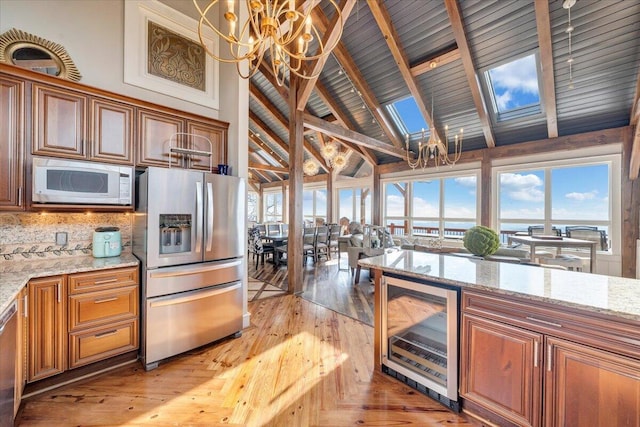 kitchen featuring appliances with stainless steel finishes, light stone counters, high vaulted ceiling, a chandelier, and wine cooler