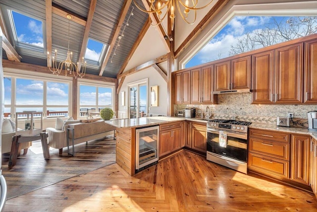 kitchen with light stone countertops, stainless steel gas range oven, high vaulted ceiling, a notable chandelier, and wine cooler