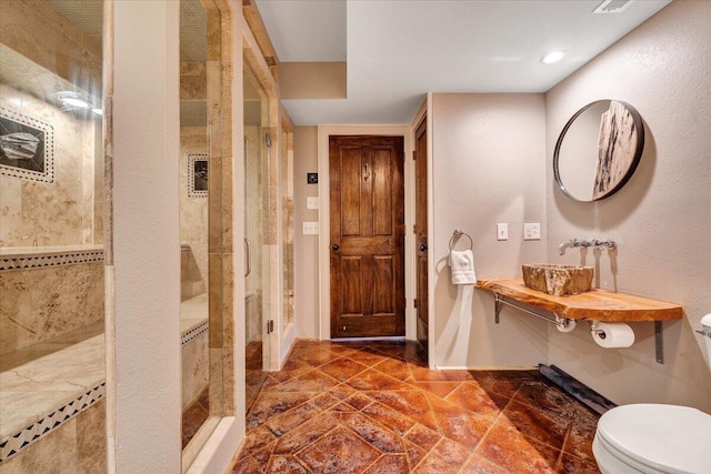 bathroom with a tile shower, toilet, and sink