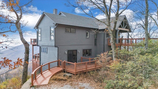 rear view of property with a deck with mountain view and a balcony