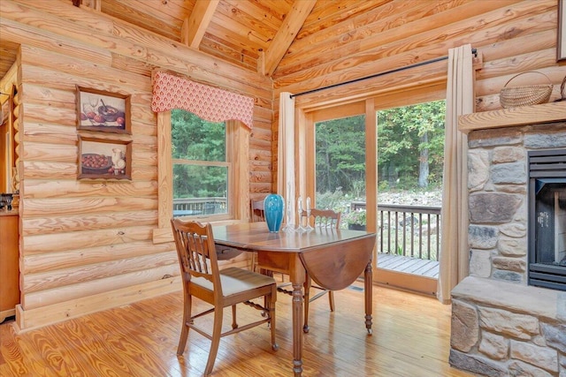 dining room with a stone fireplace, a wealth of natural light, light hardwood / wood-style flooring, and vaulted ceiling with beams