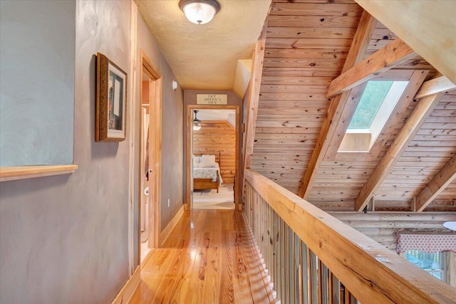 corridor with light wood-type flooring, vaulted ceiling with skylight, and wood ceiling