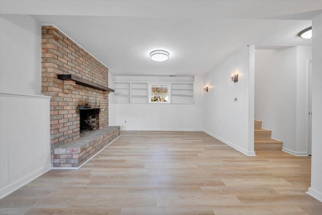 unfurnished living room with built in shelves, light hardwood / wood-style flooring, and a brick fireplace