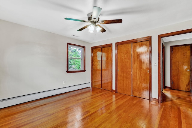 unfurnished bedroom featuring ceiling fan, light wood-type flooring, baseboard heating, and multiple closets