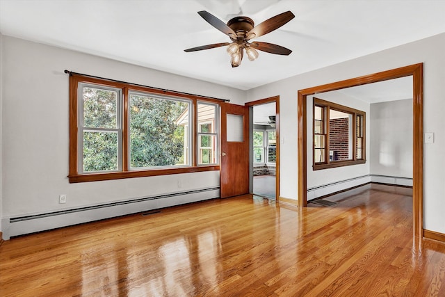 spare room with light wood-type flooring, a baseboard radiator, ceiling fan, and a healthy amount of sunlight