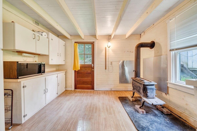 interior space featuring white cabinets, light wood-type flooring, a wood stove, and plenty of natural light