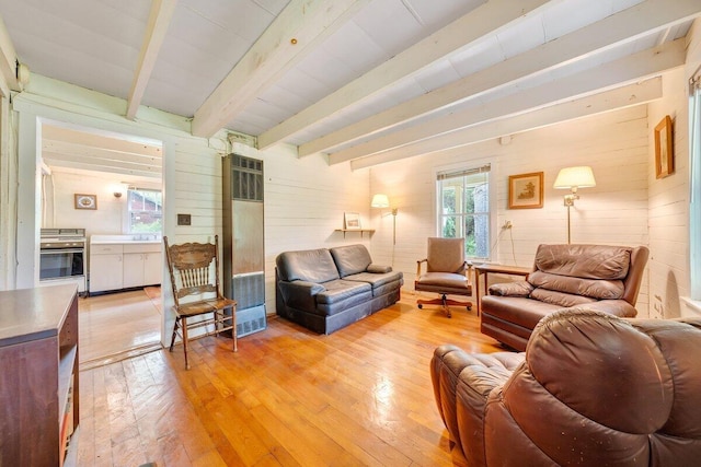 living room with beamed ceiling, light hardwood / wood-style flooring, a wealth of natural light, and wood walls