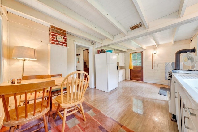 dining room with beamed ceiling, wood walls, and light wood-type flooring