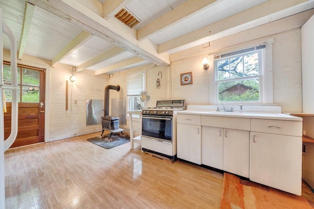 kitchen with beamed ceiling, white stove, light hardwood / wood-style flooring, and a wood stove