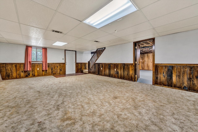 basement featuring carpet, a drop ceiling, and wood walls