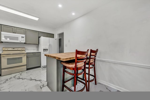 kitchen featuring gray cabinetry, wood counters, a kitchen bar, and white appliances