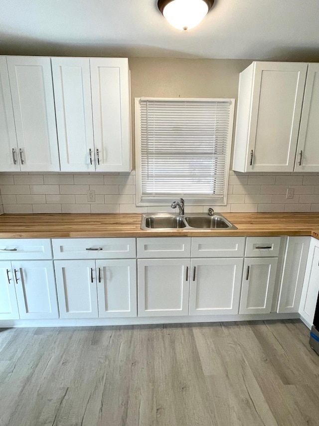 kitchen with butcher block countertops, white cabinetry, light hardwood / wood-style floors, and sink