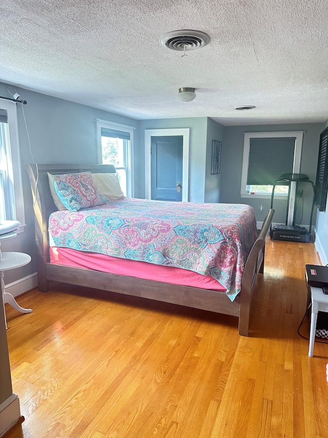 bedroom with visible vents, a textured ceiling, baseboards, and wood finished floors