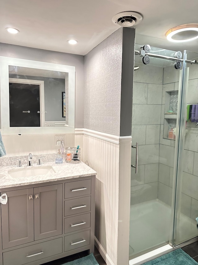 full bathroom featuring visible vents, vanity, wainscoting, and a shower stall