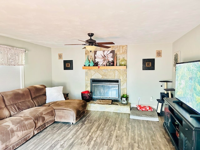 living room featuring ceiling fan, baseboards, a stone fireplace, and wood finished floors