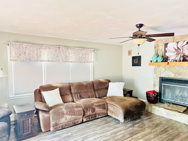 living area featuring a stone fireplace, wood finished floors, and a ceiling fan