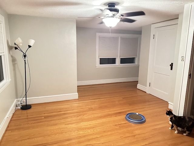 workout room with ceiling fan, baseboards, light wood finished floors, and a textured ceiling