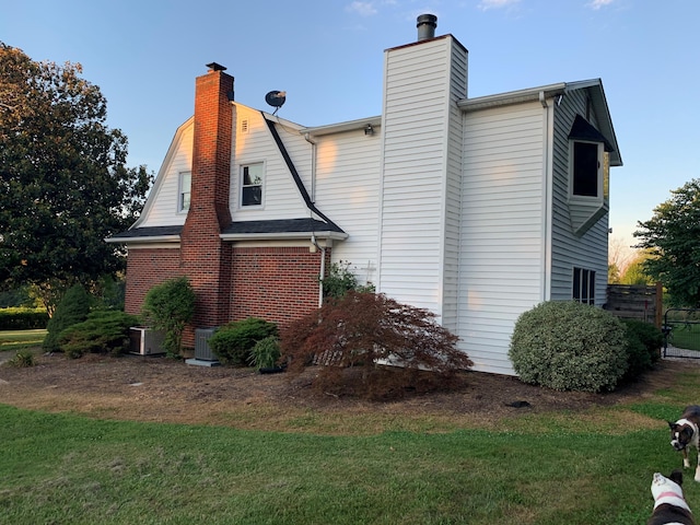 view of home's exterior with a yard, central AC unit, brick siding, and a chimney