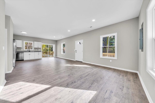 unfurnished living room featuring plenty of natural light, electric panel, and light hardwood / wood-style flooring