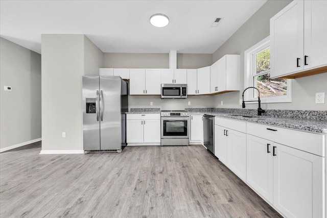 kitchen with white cabinets, appliances with stainless steel finishes, light wood-type flooring, and light stone counters