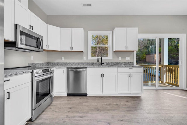 kitchen with white cabinetry, light stone countertops, stainless steel appliances, and a wealth of natural light