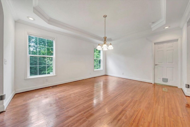 empty room featuring a chandelier, light wood-type flooring, a raised ceiling, and crown molding