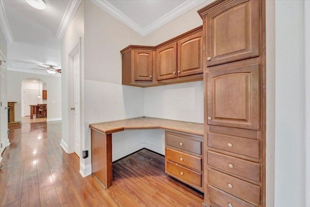 unfurnished office with ceiling fan, light hardwood / wood-style floors, built in desk, and crown molding