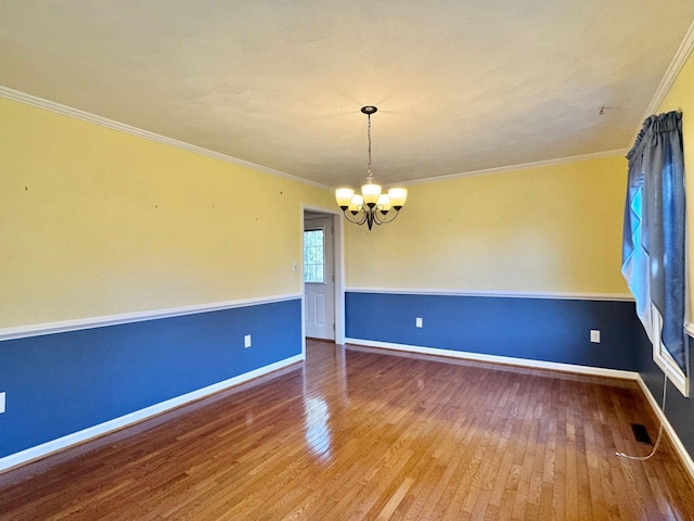 spare room with hardwood / wood-style floors, an inviting chandelier, and ornamental molding