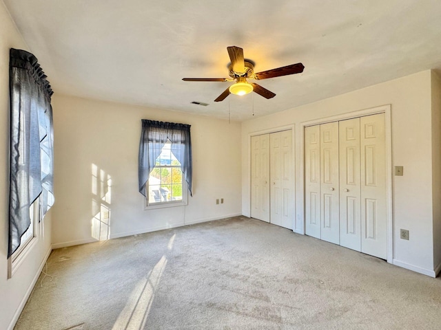 unfurnished bedroom with ceiling fan, light colored carpet, and two closets