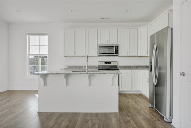 kitchen with white cabinetry, light stone counters, appliances with stainless steel finishes, a kitchen breakfast bar, and an island with sink