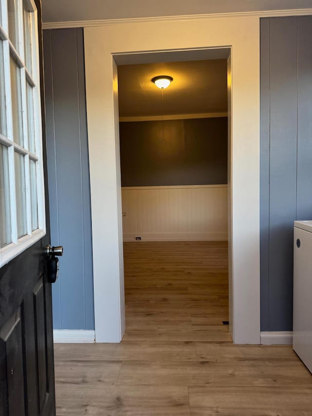 corridor with light wood-type flooring and crown molding