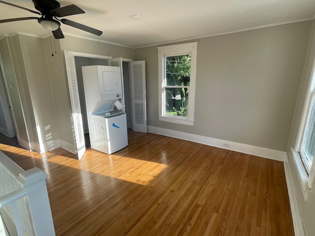 unfurnished bedroom featuring ornamental molding, hardwood / wood-style flooring, ceiling fan, and stacked washer and clothes dryer