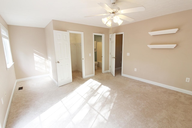 unfurnished bedroom with a walk in closet, ensuite bathroom, light colored carpet, ceiling fan, and a closet