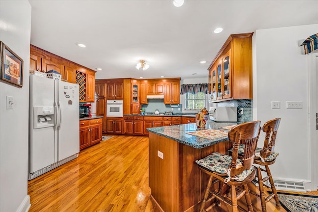 kitchen with a breakfast bar, white appliances, backsplash, light hardwood / wood-style flooring, and kitchen peninsula